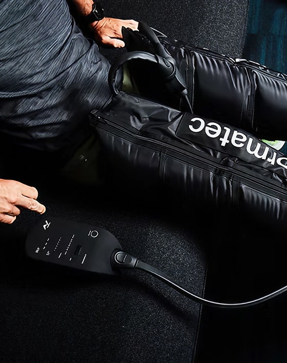 A person using a muscular recovery treatment device, with black sleeves covering their legs, and a remote control in hand.